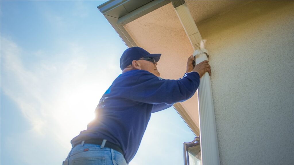 Technician securing and cleaning a gutter downspout as part of gutter guard and gutter cleaning services in Southern California