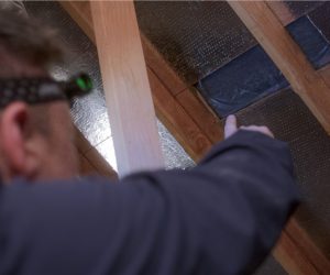 Technician inspecting attic vent opening for ember intrusion and fire risk during home hardening services in Southern California