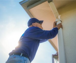 Technician securing and cleaning a gutter downspout as part of gutter guard and gutter cleaning services in Southern California