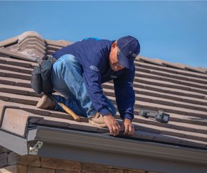 Technician installing gutter guards and cleaning roof gutters on a residential home in Southern California